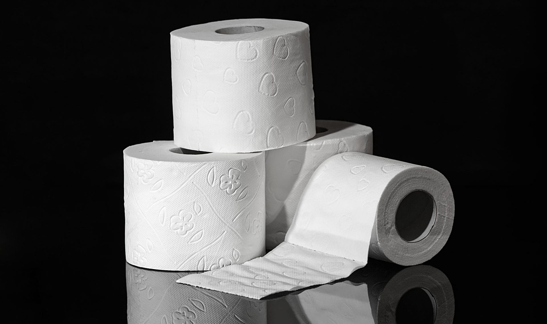 3 Rollen Toilettenpapier stehend und eine Rolle Toilettenpapier liegend abgerollt auf schwarzem Hintergrund 3 Rollen Toilettenpapier stehend und eine Rolle Toilettenpapier liegend abgerollt auf schwarzem Hintergrund