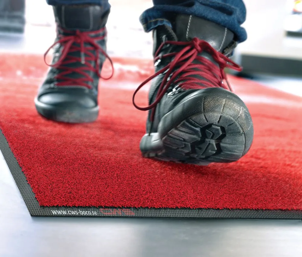 Arbeitsschuhe mit roten Schnürsenkeln auf roter Schmutzfangmatte Arbeitsschuhe mit roten Schnürsenkeln auf roter Schmutzfangmatte - Schmutzfangmatten mieten