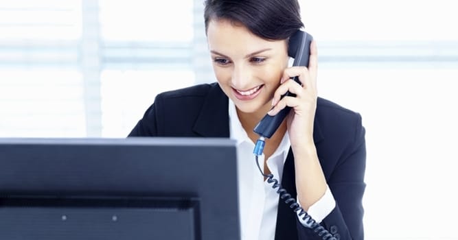 Telefonierende Frau, die auf einen Monitor blickt